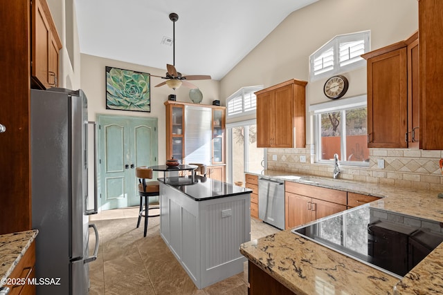 kitchen featuring tasteful backsplash, appliances with stainless steel finishes, a kitchen island, ceiling fan, and light stone countertops