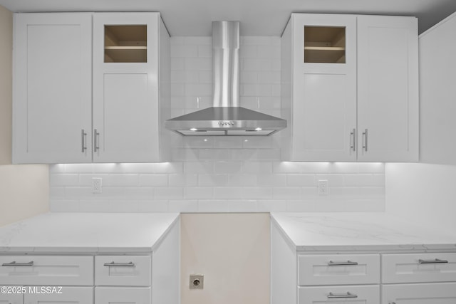 kitchen with light stone counters, wall chimney range hood, backsplash, and white cabinets