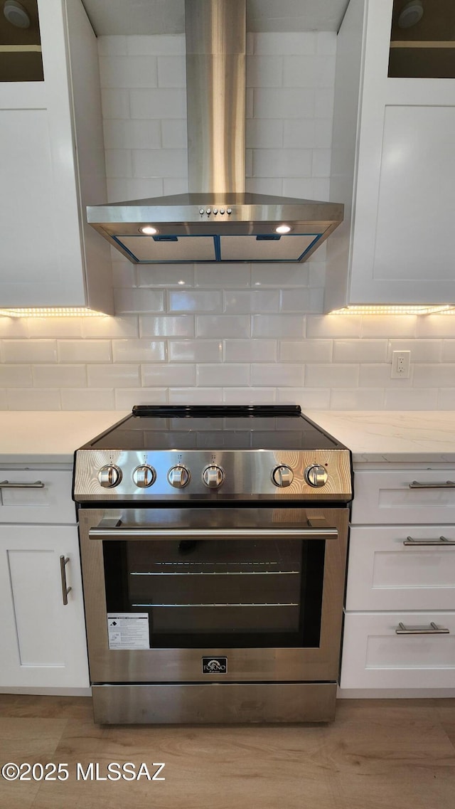 kitchen with tasteful backsplash, white cabinetry, high end stainless steel range, light wood-type flooring, and wall chimney exhaust hood