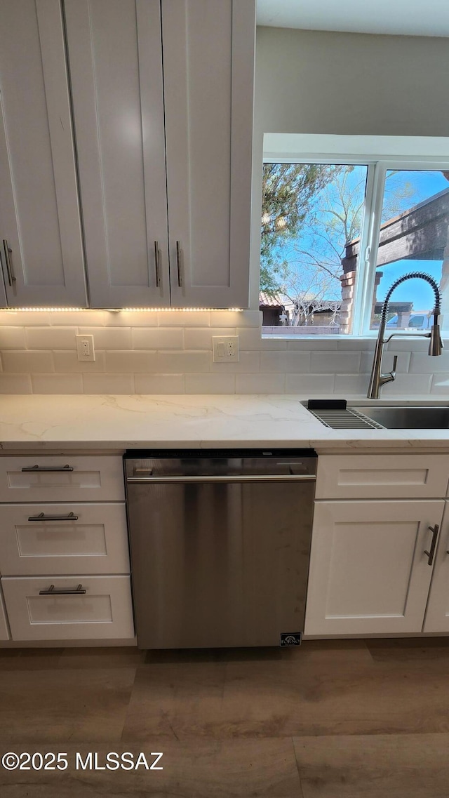 kitchen featuring light stone countertops, sink, stainless steel dishwasher, and white cabinets