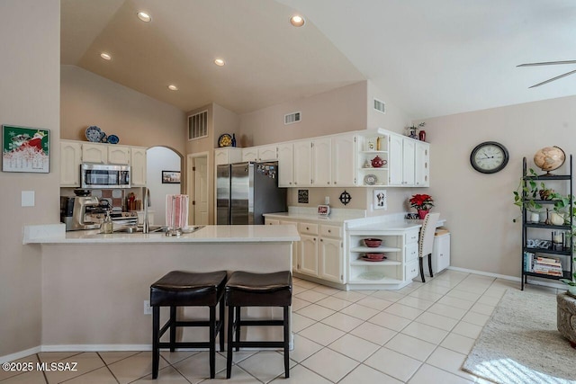 kitchen featuring white cabinetry, stainless steel appliances, kitchen peninsula, a kitchen bar, and light tile patterned floors