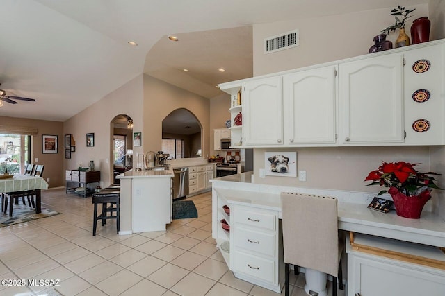 kitchen featuring kitchen peninsula, vaulted ceiling, a kitchen bar, white cabinets, and appliances with stainless steel finishes