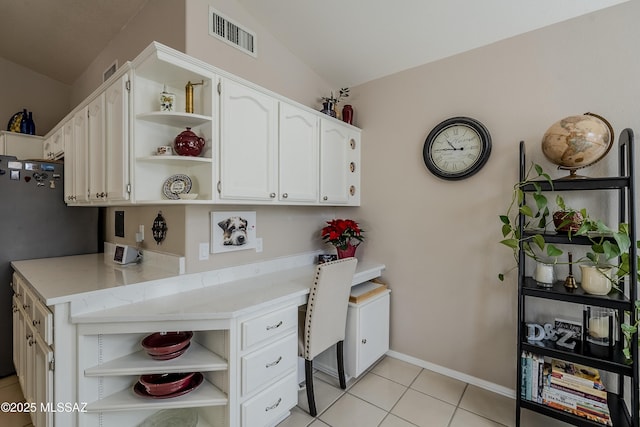 kitchen with white cabinetry, black refrigerator, light tile patterned floors, and vaulted ceiling