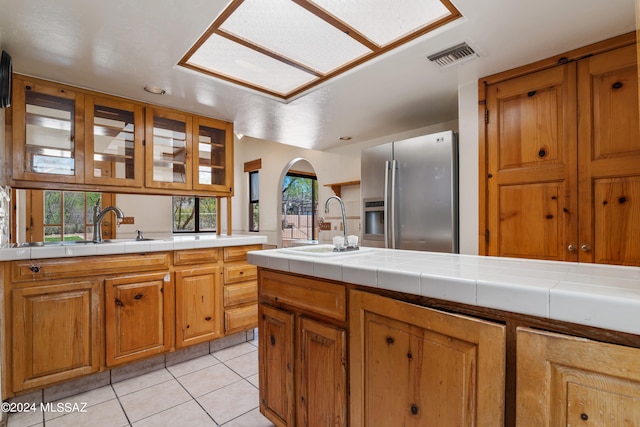 kitchen featuring stainless steel refrigerator with ice dispenser, light tile patterned floors, tile counters, and sink