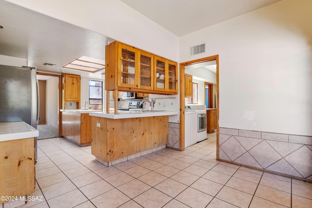 kitchen featuring kitchen peninsula, stainless steel fridge, sink, light tile patterned floors, and washer / clothes dryer