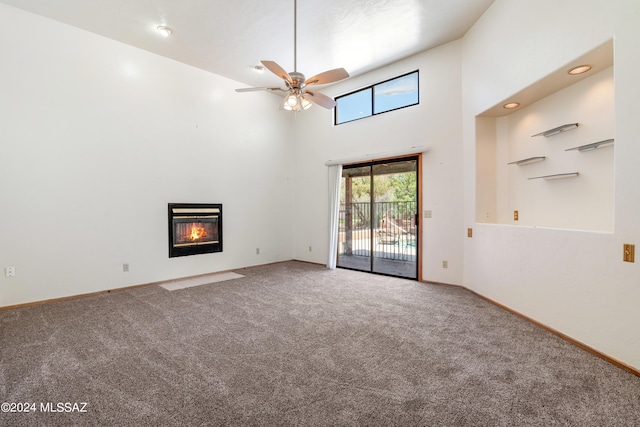 unfurnished living room featuring carpet flooring, ceiling fan, and a towering ceiling