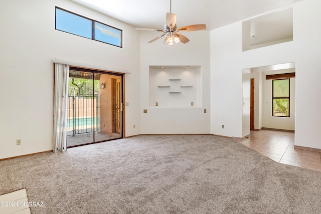 unfurnished living room featuring ceiling fan, a towering ceiling, and light colored carpet