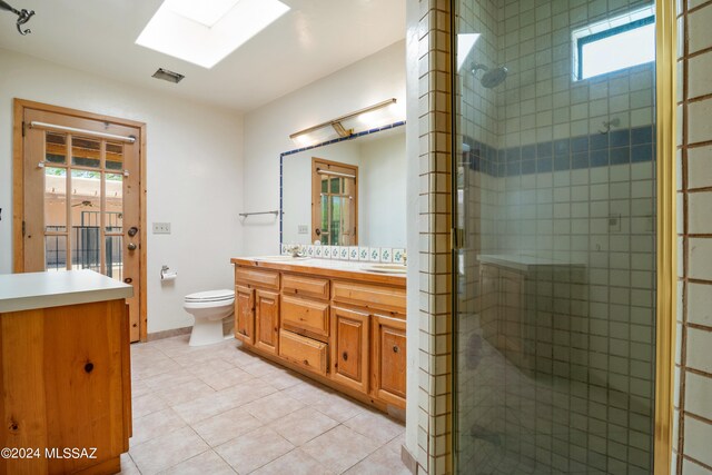 bathroom with a skylight, tile patterned floors, vanity, toilet, and a shower with shower door