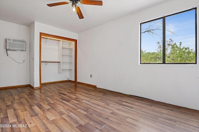 unfurnished bedroom with a wall mounted AC, ceiling fan, a closet, and wood-type flooring