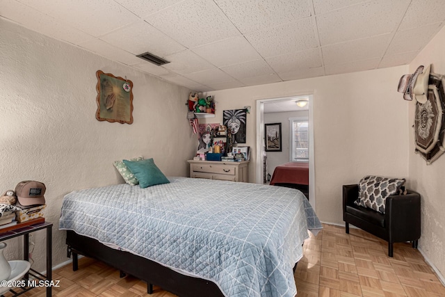 bedroom featuring a drop ceiling and light parquet floors