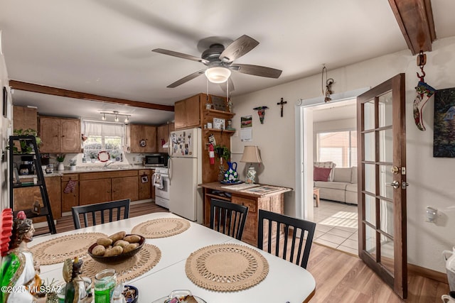 dining room featuring light wood-type flooring, ceiling fan, french doors, beam ceiling, and sink