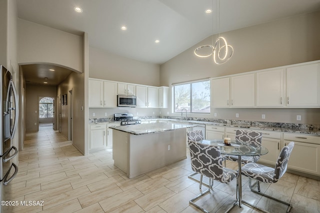 kitchen featuring light stone countertops, appliances with stainless steel finishes, high vaulted ceiling, white cabinets, and a center island