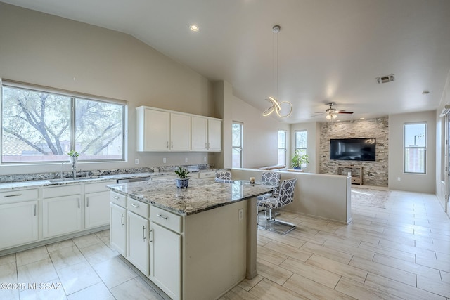 kitchen featuring lofted ceiling, white cabinets, ceiling fan, light stone countertops, and a kitchen island