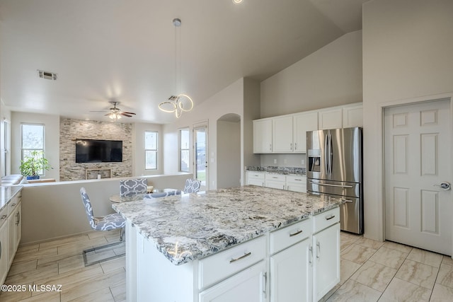 kitchen with white cabinetry, a center island, ceiling fan, stainless steel fridge, and decorative light fixtures