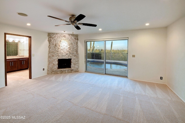 unfurnished living room with light colored carpet, a stone fireplace, and ceiling fan