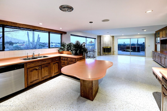 kitchen with sink, hanging light fixtures, stainless steel dishwasher, decorative backsplash, and a fireplace