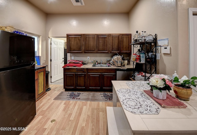 kitchen with tile countertops, black refrigerator, light wood-type flooring, and sink