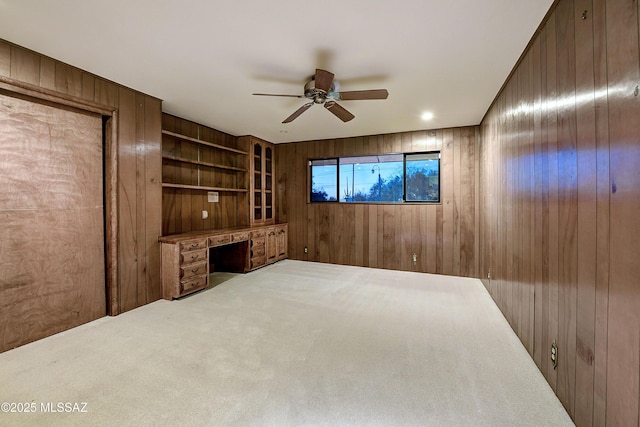 interior space featuring ceiling fan, built in desk, and wood walls