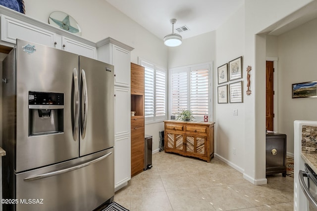 kitchen featuring white cabinets, stainless steel fridge, light stone counters, and light tile patterned floors