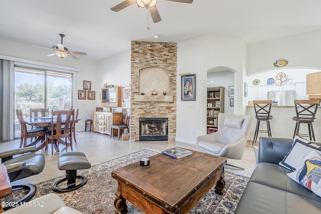 living room with a stone fireplace, ceiling fan, and light tile patterned flooring