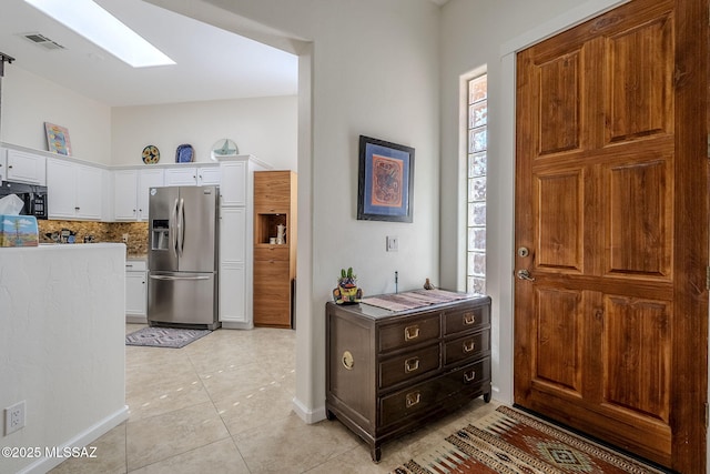 kitchen featuring a skylight, light tile patterned floors, stainless steel fridge with ice dispenser, backsplash, and white cabinets