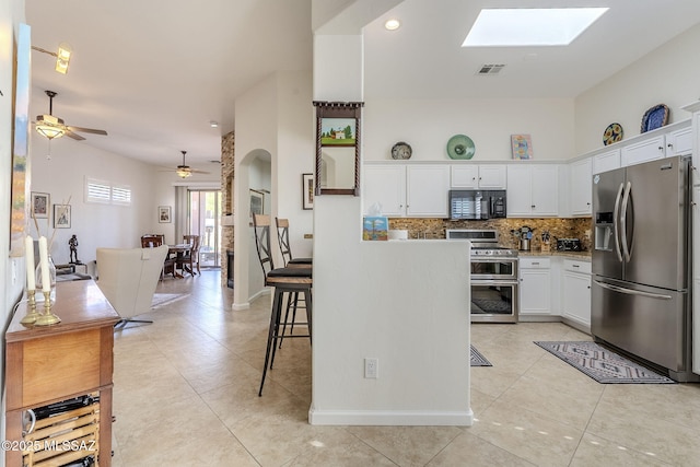 kitchen featuring a skylight, white cabinetry, ceiling fan, tasteful backsplash, and appliances with stainless steel finishes