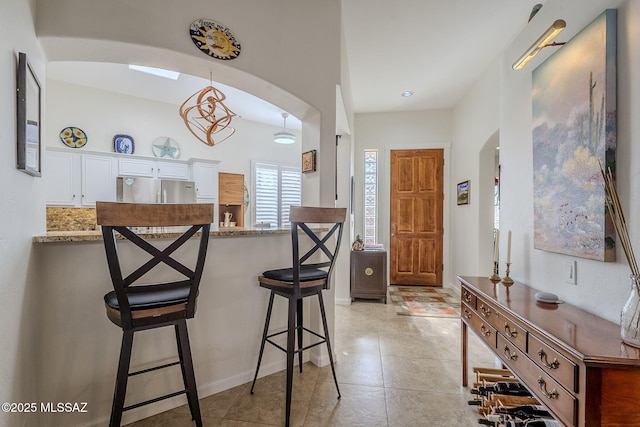 kitchen with a breakfast bar, light tile patterned floors, light stone counters, white cabinetry, and stainless steel refrigerator