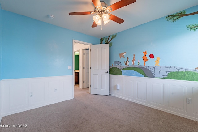 unfurnished bedroom featuring a wainscoted wall, carpet, and a ceiling fan