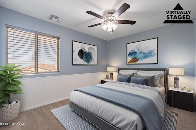 bedroom with a wainscoted wall, ceiling fan, carpet flooring, and visible vents