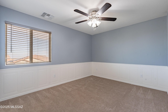 unfurnished room with a wainscoted wall, carpet, visible vents, and ceiling fan