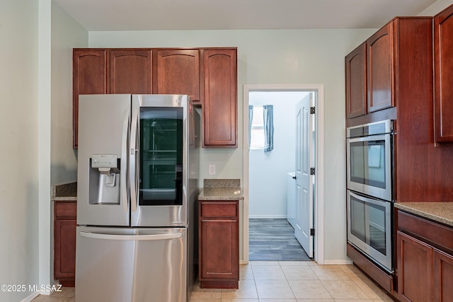 kitchen with light tile patterned floors, baseboards, appliances with stainless steel finishes, and light stone counters