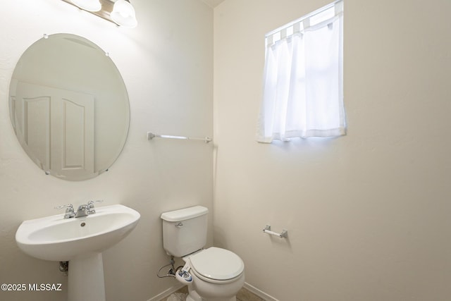 half bathroom with baseboards, a sink, and toilet