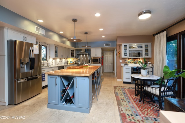 kitchen featuring white cabinetry, a center island, hanging light fixtures, stainless steel appliances, and wood counters