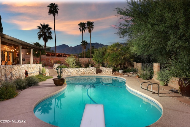 pool at dusk featuring a mountain view, a patio, and a diving board