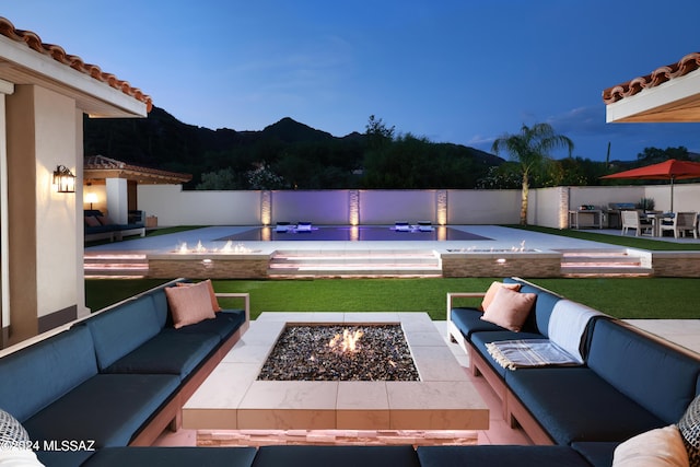 pool at dusk with a mountain view, a patio, and an outdoor living space with a fire pit