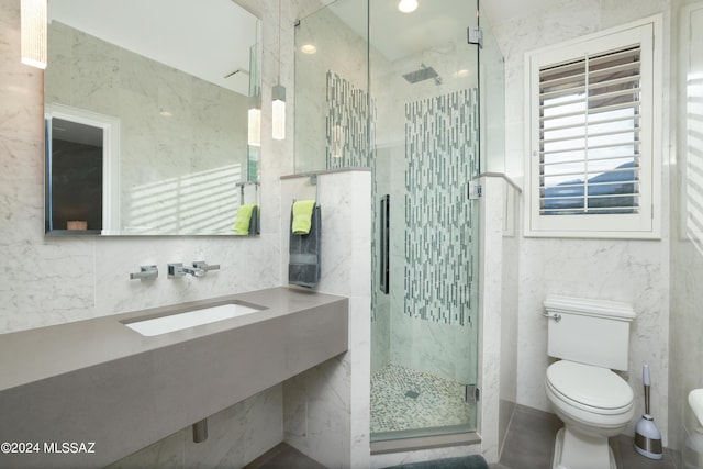 bathroom with sink, a shower with door, tile walls, and toilet