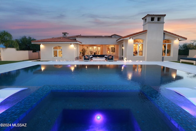 pool at dusk with an in ground hot tub, an outdoor hangout area, and a patio area