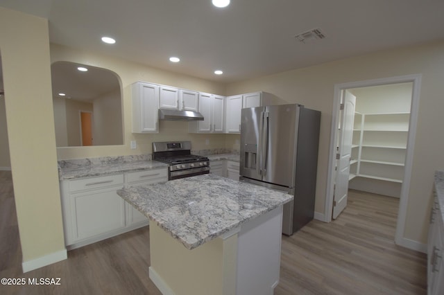 kitchen with light stone countertops, stainless steel appliances, a kitchen island, light hardwood / wood-style flooring, and white cabinetry