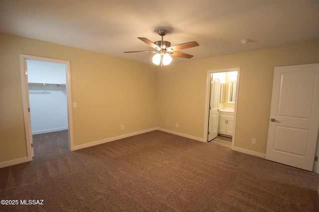 unfurnished bedroom with ensuite bathroom, ceiling fan, dark colored carpet, a spacious closet, and a closet