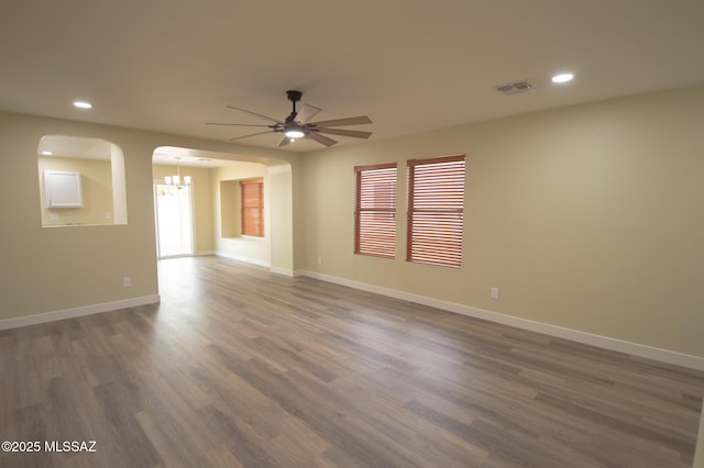 empty room with ceiling fan with notable chandelier and dark wood-type flooring