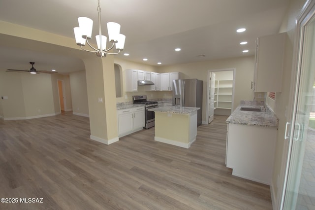 kitchen with white cabinetry, stainless steel appliances, light stone counters, decorative light fixtures, and ceiling fan with notable chandelier