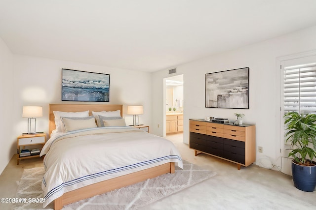 bedroom with visible vents, light colored carpet, and ensuite bath