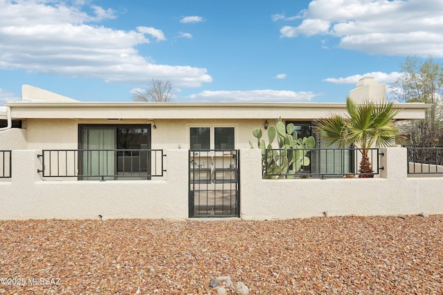 back of property featuring a gate, a fenced front yard, a chimney, and stucco siding