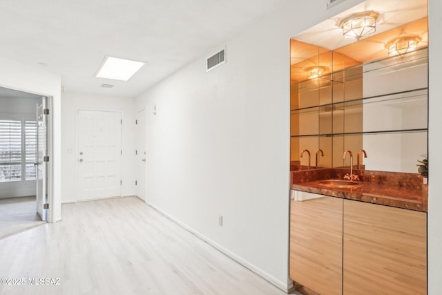 bar featuring visible vents, a sink, light wood-style floors, indoor wet bar, and baseboards