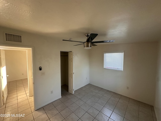 unfurnished bedroom featuring light tile patterned floors, a textured ceiling, a closet, and ceiling fan