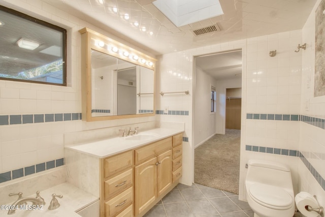 bathroom with tile walls, tile patterned flooring, a skylight, vanity, and toilet