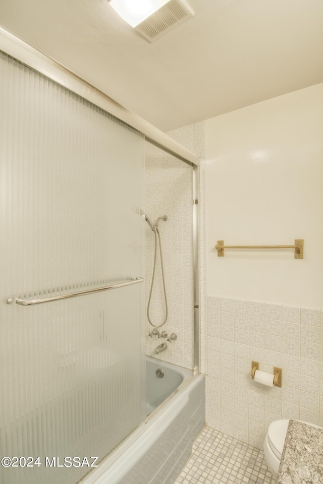 bathroom with tile walls, tile patterned floors, enclosed tub / shower combo, and toilet