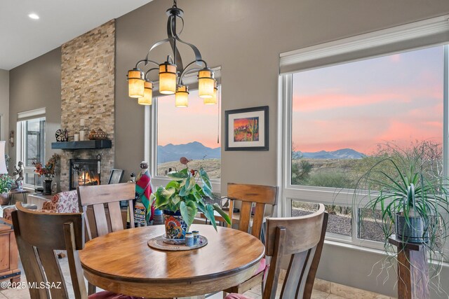 dining room featuring ceiling fan with notable chandelier, a stone fireplace, a wealth of natural light, and light tile patterned flooring