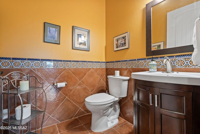 bathroom featuring tile patterned flooring, toilet, vanity, tile walls, and wainscoting
