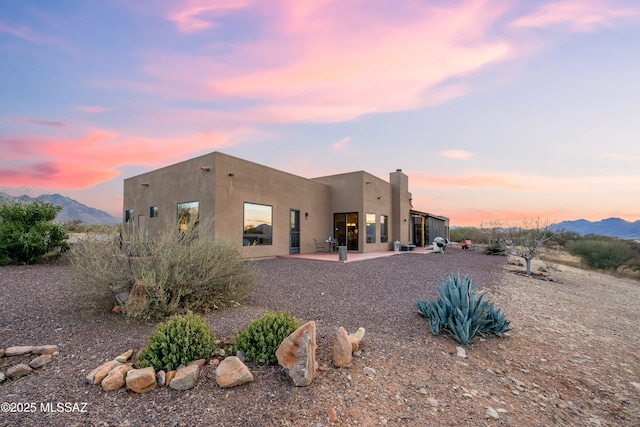 back house at dusk with a mountain view and a patio